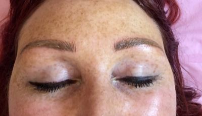 Microbladed brows on a freckled client with red-pink hair, eyes closed